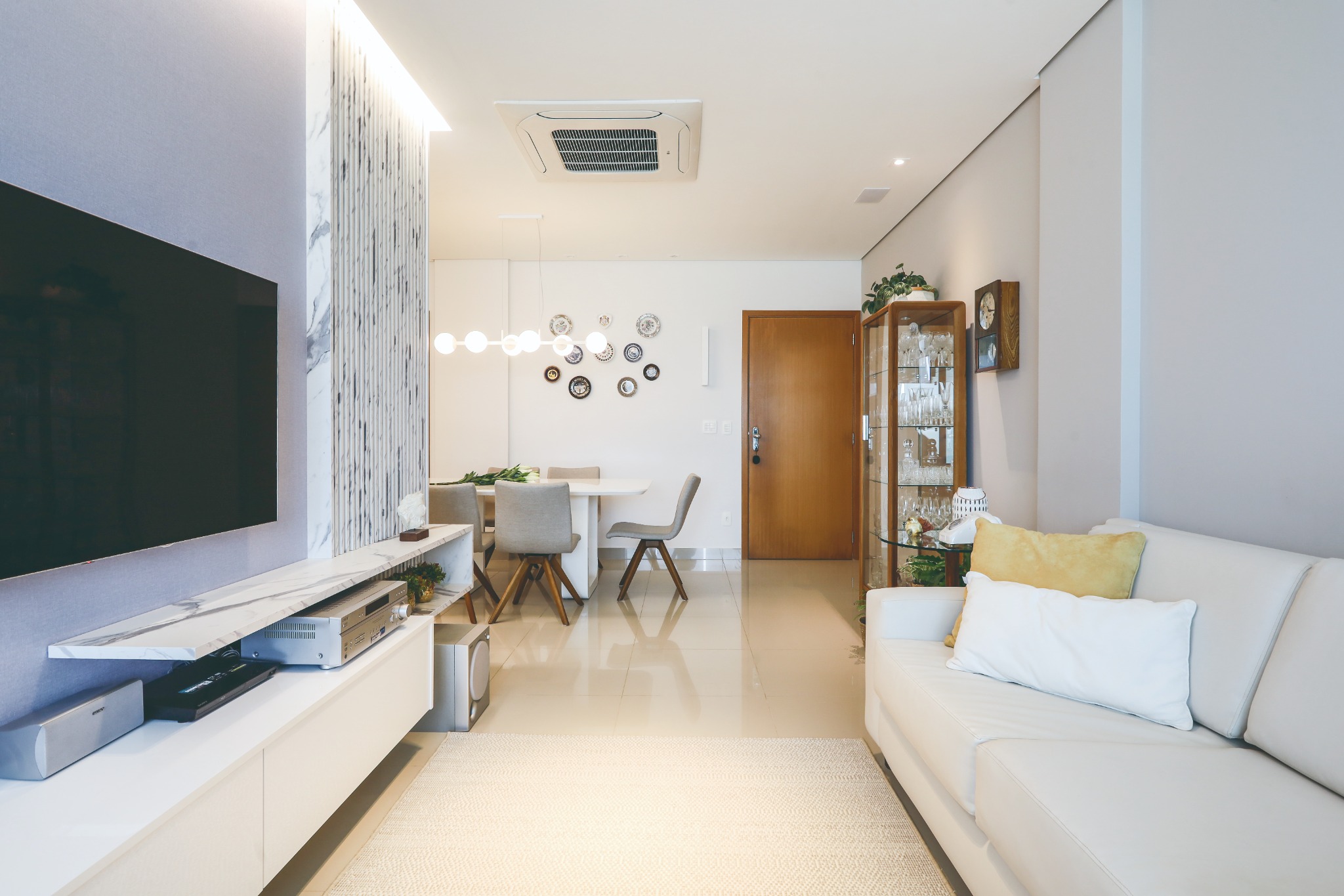 Sala de estar clara com painel de televisão e peças afetivas